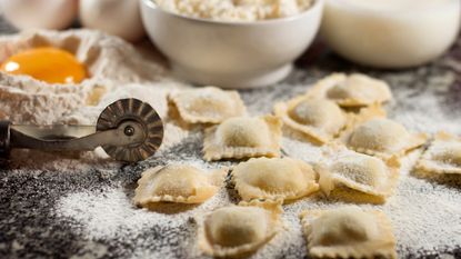 Handmade ravioli next to flour, egg yolks, and a pasta cutter