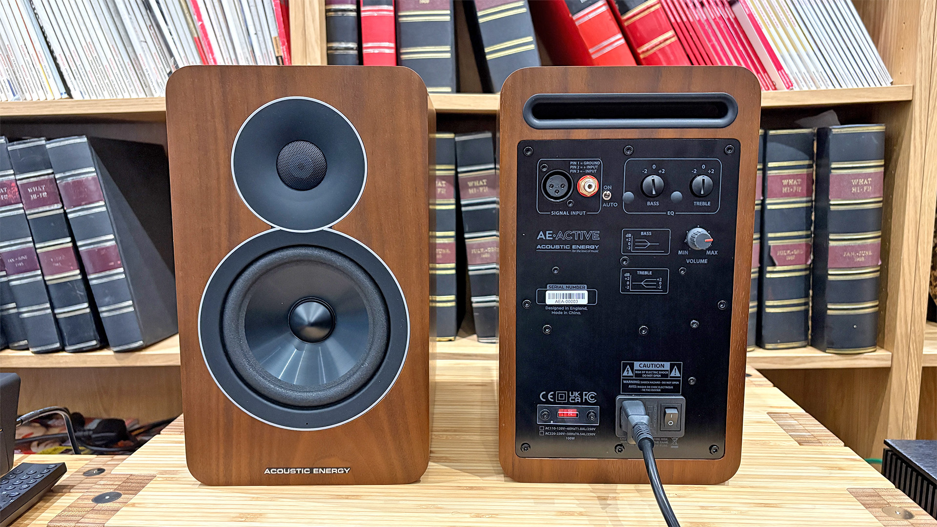 Acoustic Energy AE Active active speakers on hi-fi rack in front of bookcase, one facing away from camera