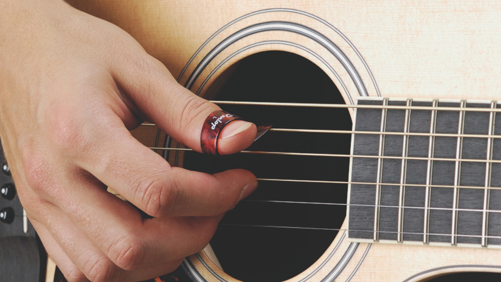 A man plays an acoustic guitar with a thumb pick