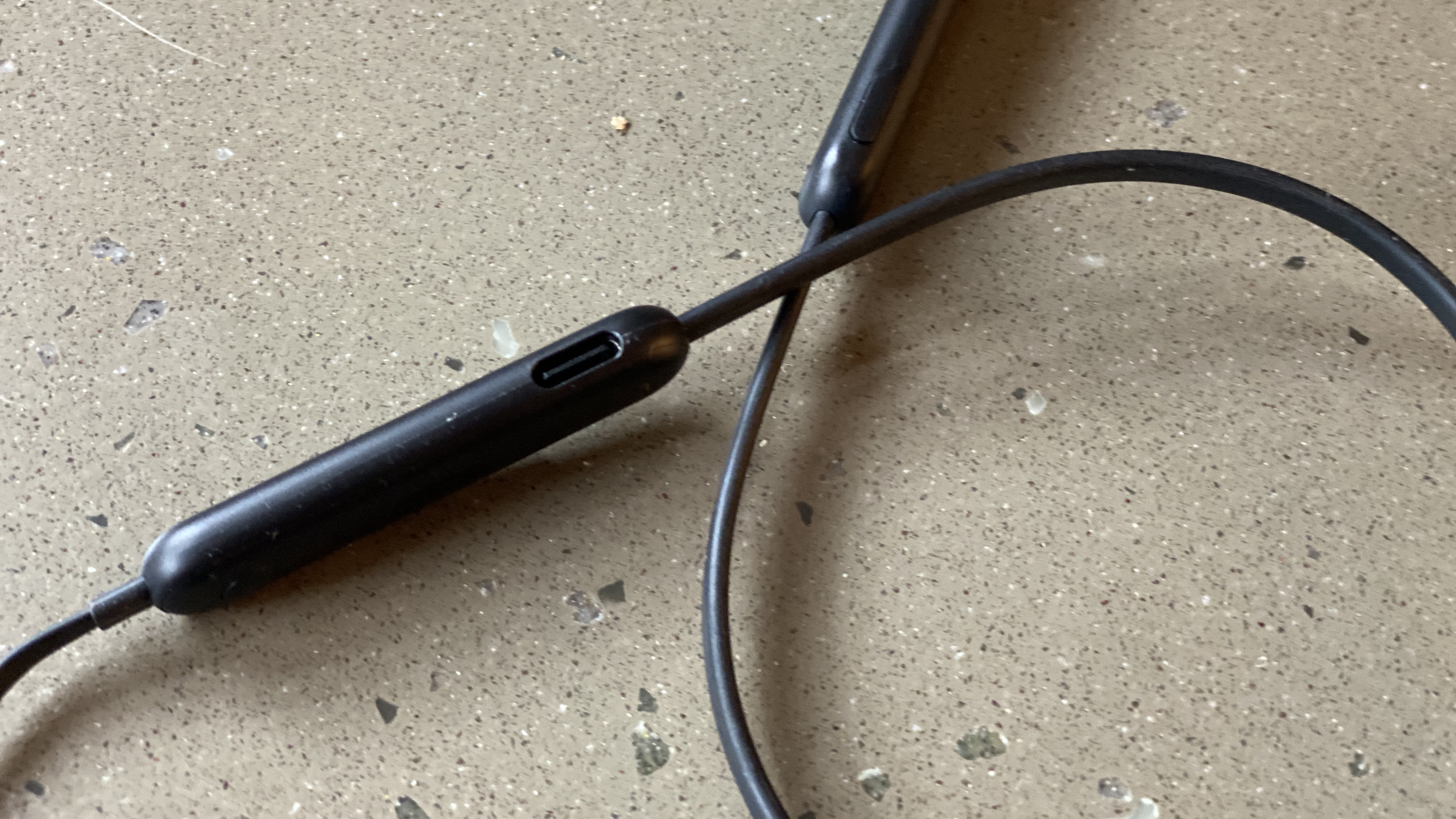 Kontrol earphone nirkabel Beats Flex berwarna hitam di atas permukaan marmer