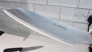 A Global knife in hand with the edge showing brilliantly in the light.