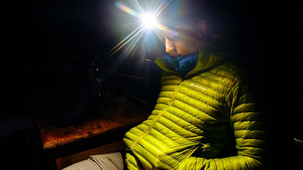 Person sitting in the dark outdoors wearing the Montane Alpine 850 Nano Jacket