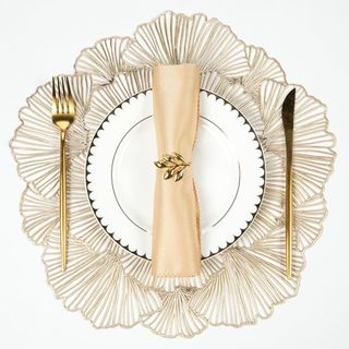 Round placemat in gold, with gold cutlery, a gold napkin with leaf holder and scalloped white china plate with gold edge