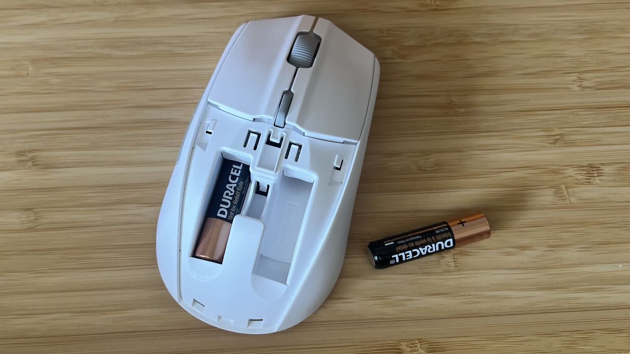 SteelSeries Rival 3 Wireless Gen 2 gaming mouse with top cover removed. One battery is in a left compartment with the right compartment staying empty, and a AAA battery is off to the side.