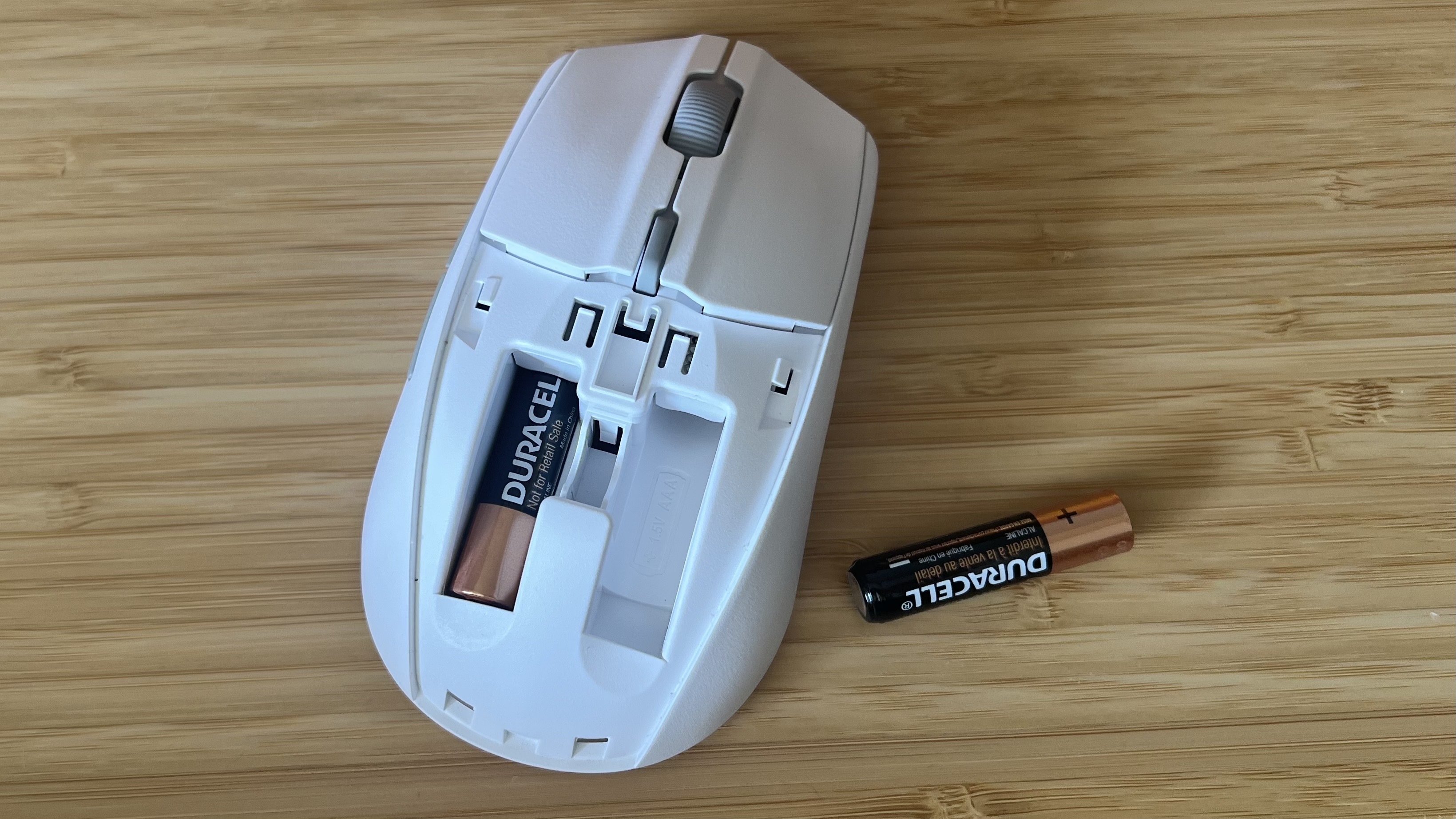 SteelSeries Rival 3 Wireless Gen 2 gaming mouse with top cover removed. One battery is in a left compartment with the right compartment staying empty, and a AAA battery is off to the side.