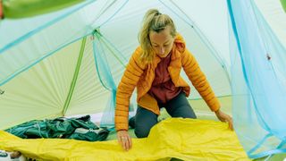 Woman lying out sleeping mat on mat in tent