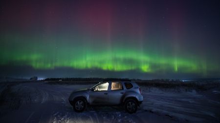 the northern lights dance over a snowy landscape with a small car in the foreground