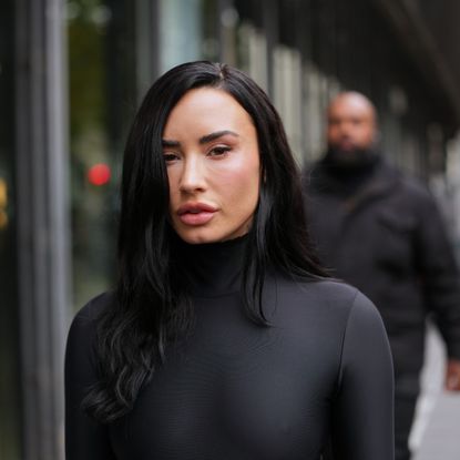 a white woman with long black hair photographed on the street wearing a black turtleneck