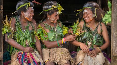 Three women wearing grass shirts and skirts sit next to each other.
