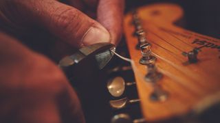 Man snips electric guitar string on Fender guitar