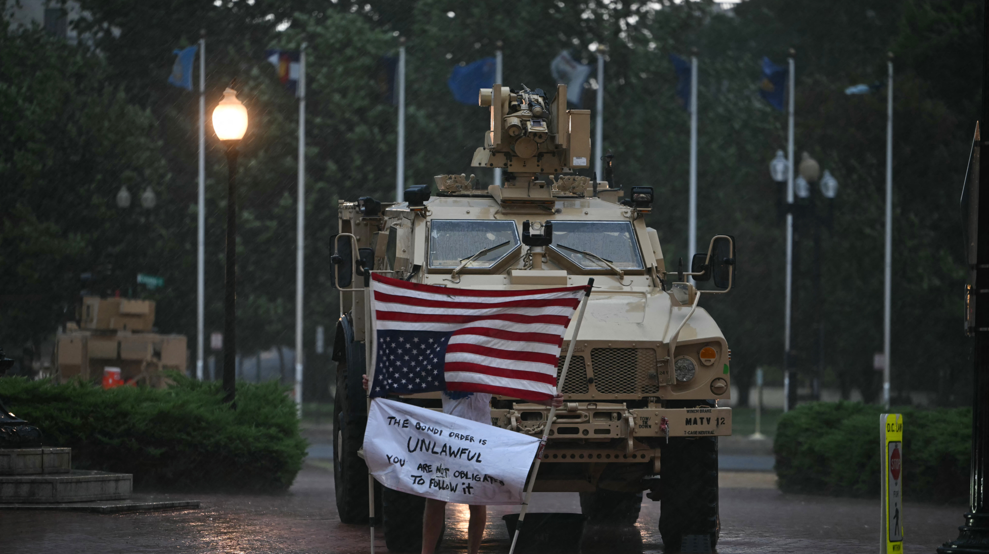 A protester is blown around in the rain as members of the DC National Guard take shelter in their vehicle, outside Union Station during a storm in Washington, DC, on August 17, 2025. US President Donald Trump on August 11 deployed military and federal law enforcement to curb violent crime in Washington, as he seeks to make good on his campaign pledge to be a "law and order" president. The Republican leader said he would place the city's Metropolitan Police under federal government control while also sending the National Guard onto the streets of the US capital. 
