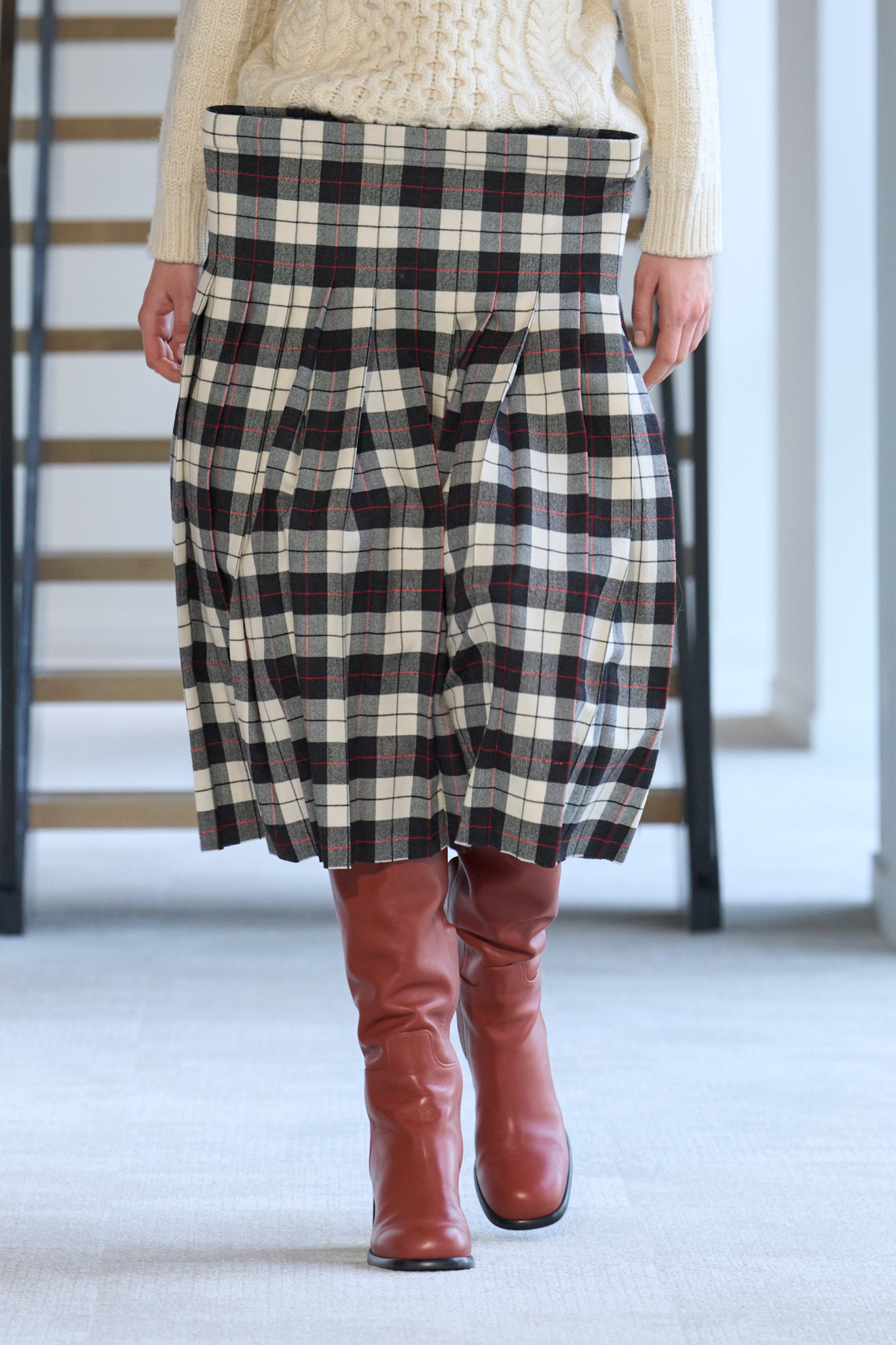 Duran Lantinkmodel wearing plaid skirt. chunky sweater, and a red boots.
