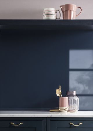 A blue aluminium backsplash in a modern navy blue kitchen with marble countertop