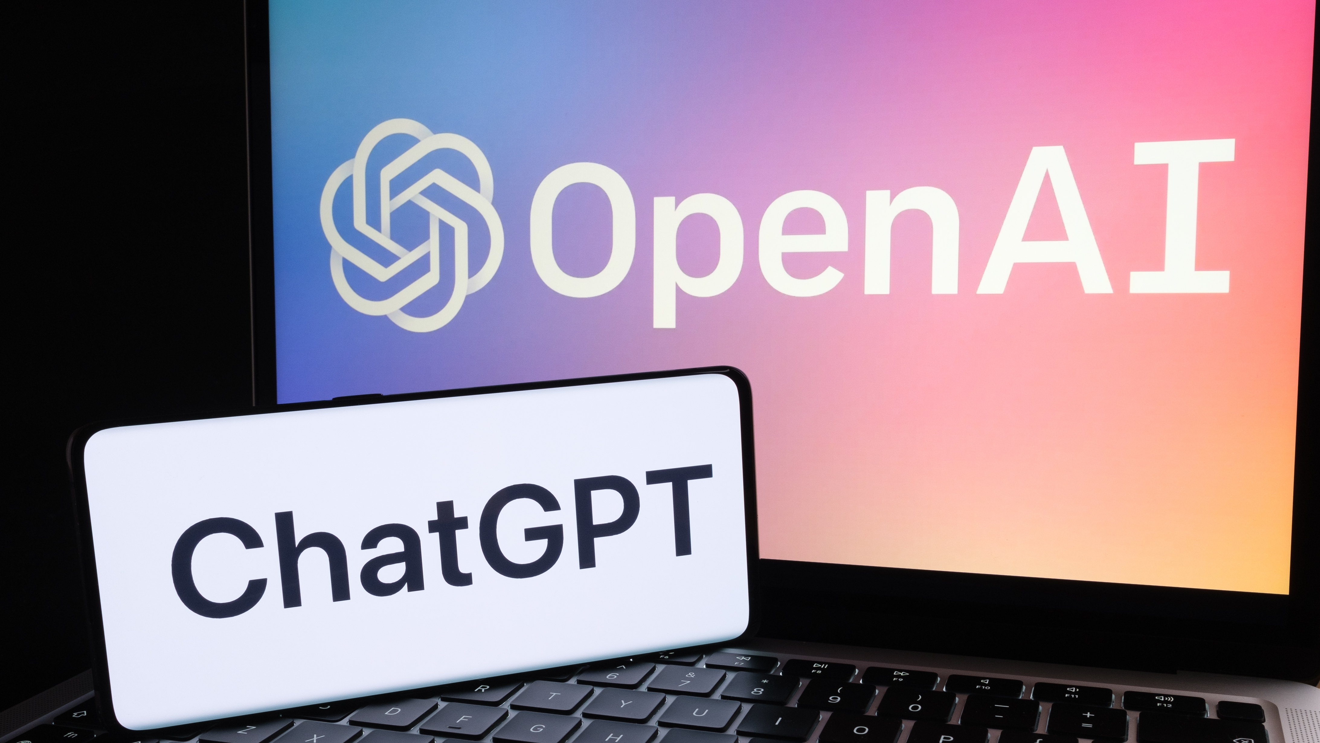Un teléfono con el logo ChatGPT y una computadora portátil con el logo OpenAI