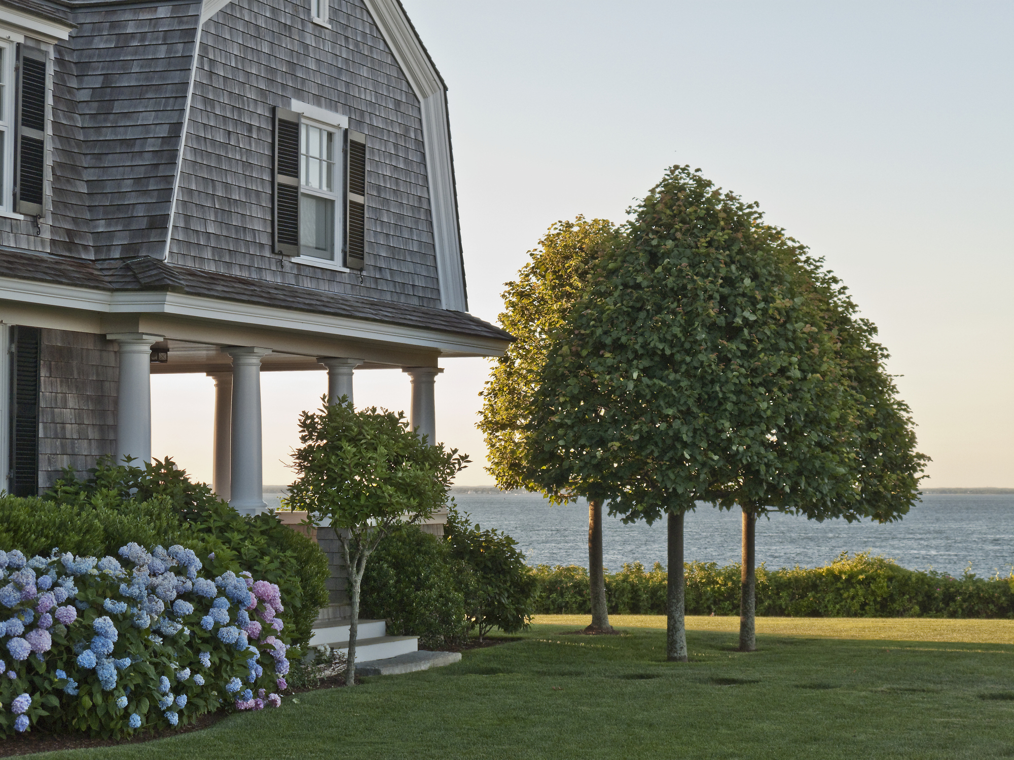 Dutch Colonial shingle style house in Vineyard Haven, Martha's Vineyard, Massachusetts. The home has a hydrangea bush and an ocean view.