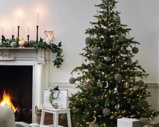 Pre-Lit Grand Spruce Christmas Tree in the corner of a living room, lit and decorated with white The White Company boxes underneath