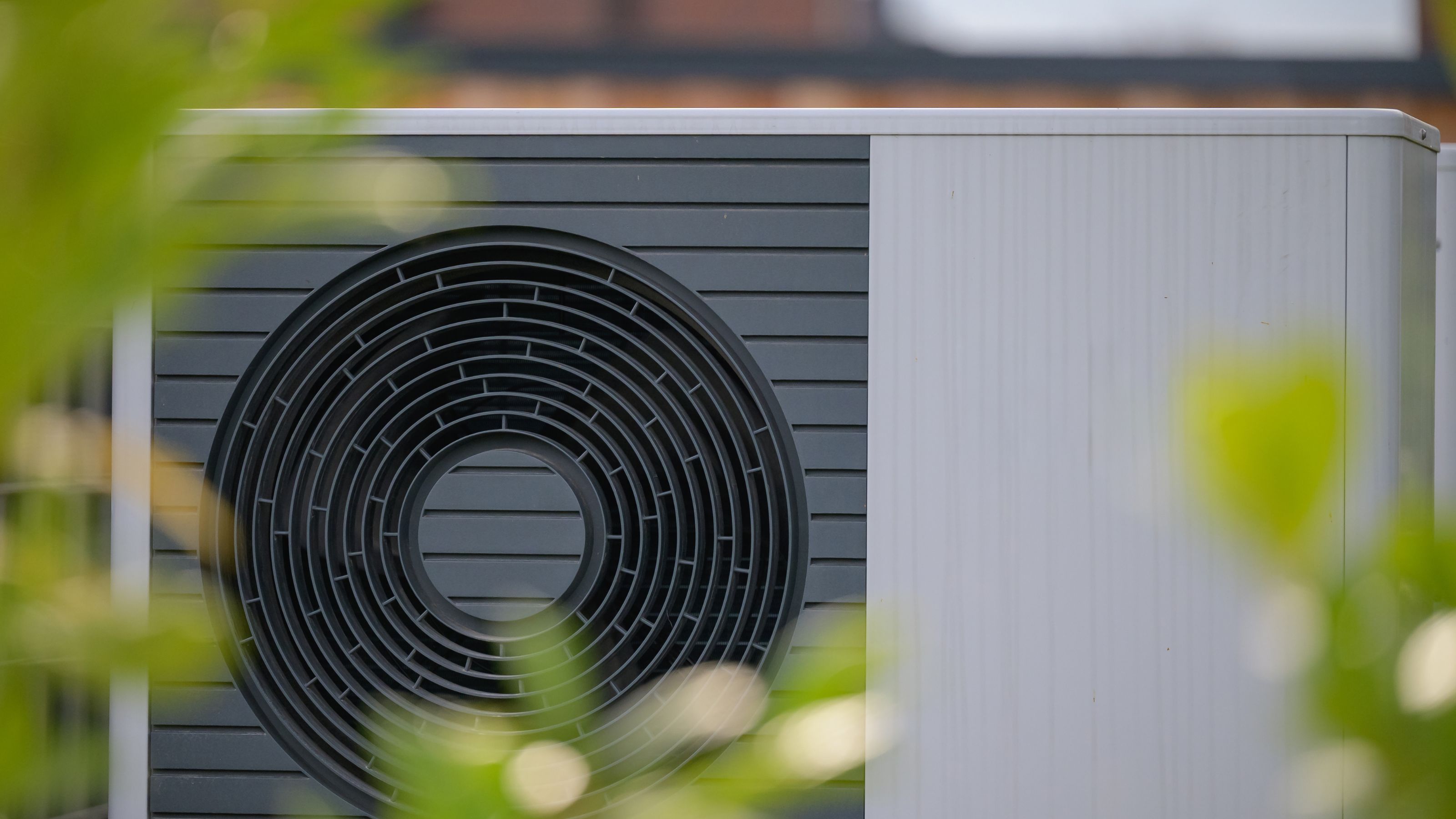 Close up of an air source heat pump through some leaves