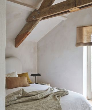 bed in room with exposed beams with limewash walls in pale pink