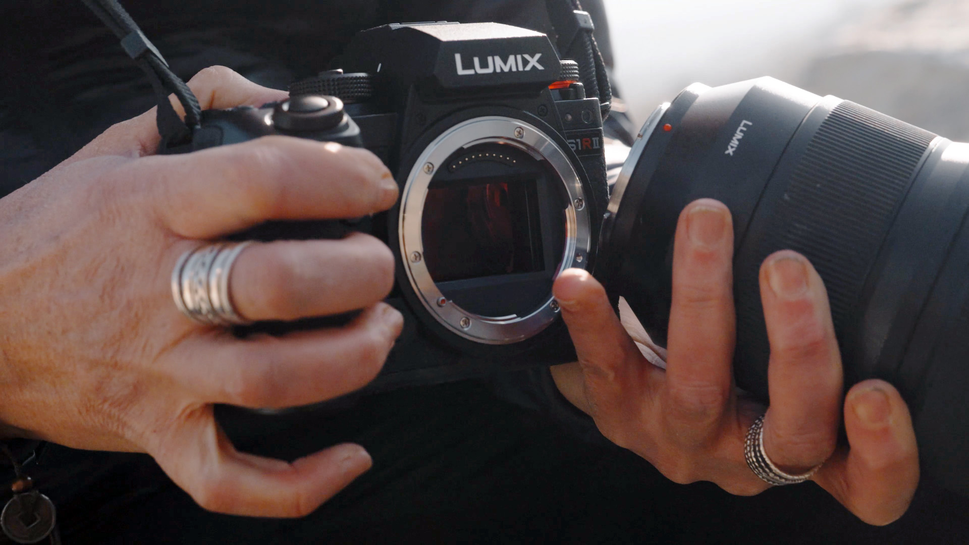 Panasonic Lumix S1R II mirrorless camera in the hand, with 24-70mm lens being attached