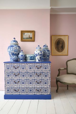 pink living room with Annie Sloan decoupage chest of drawers , blue and white ceramic pots, white painted floor, vintage armchair, vintage paintings