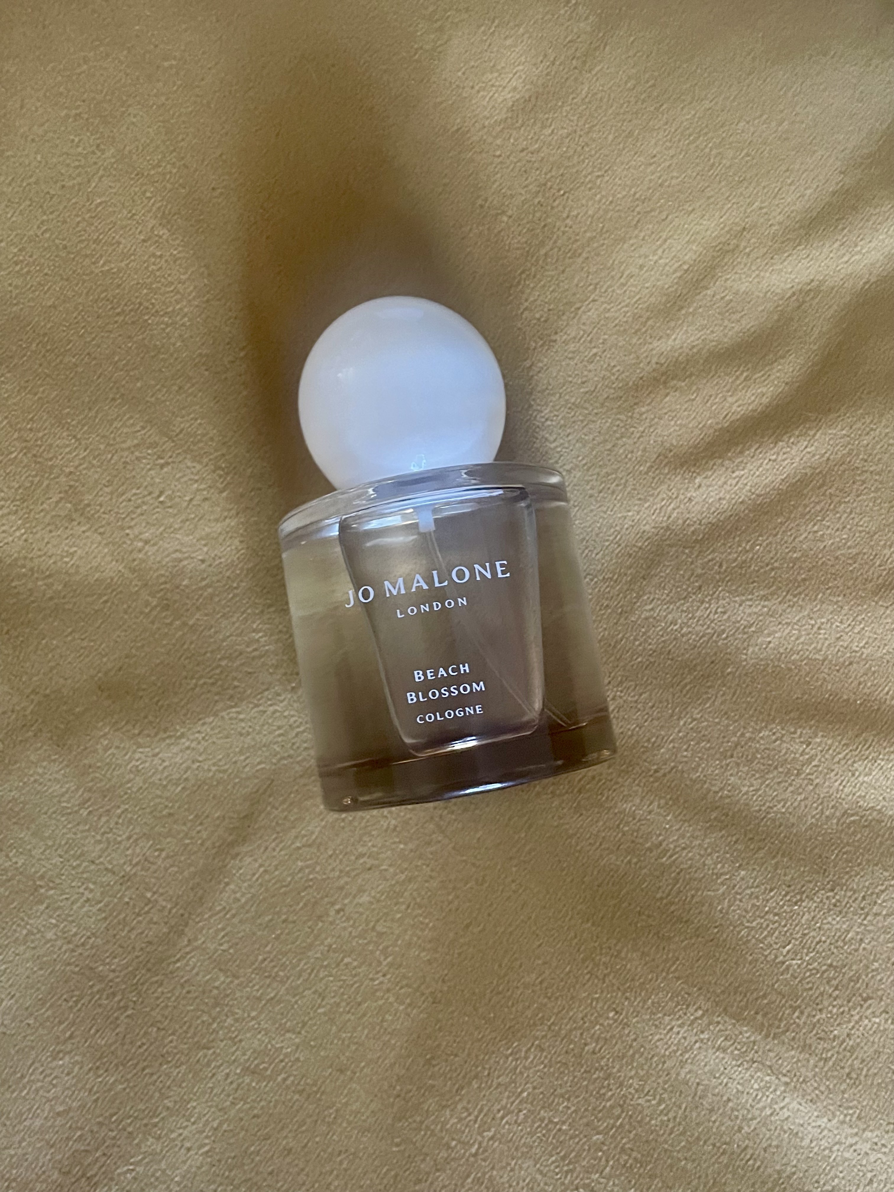 jo malone beach blossom perfume bottle on fuzzy gold background