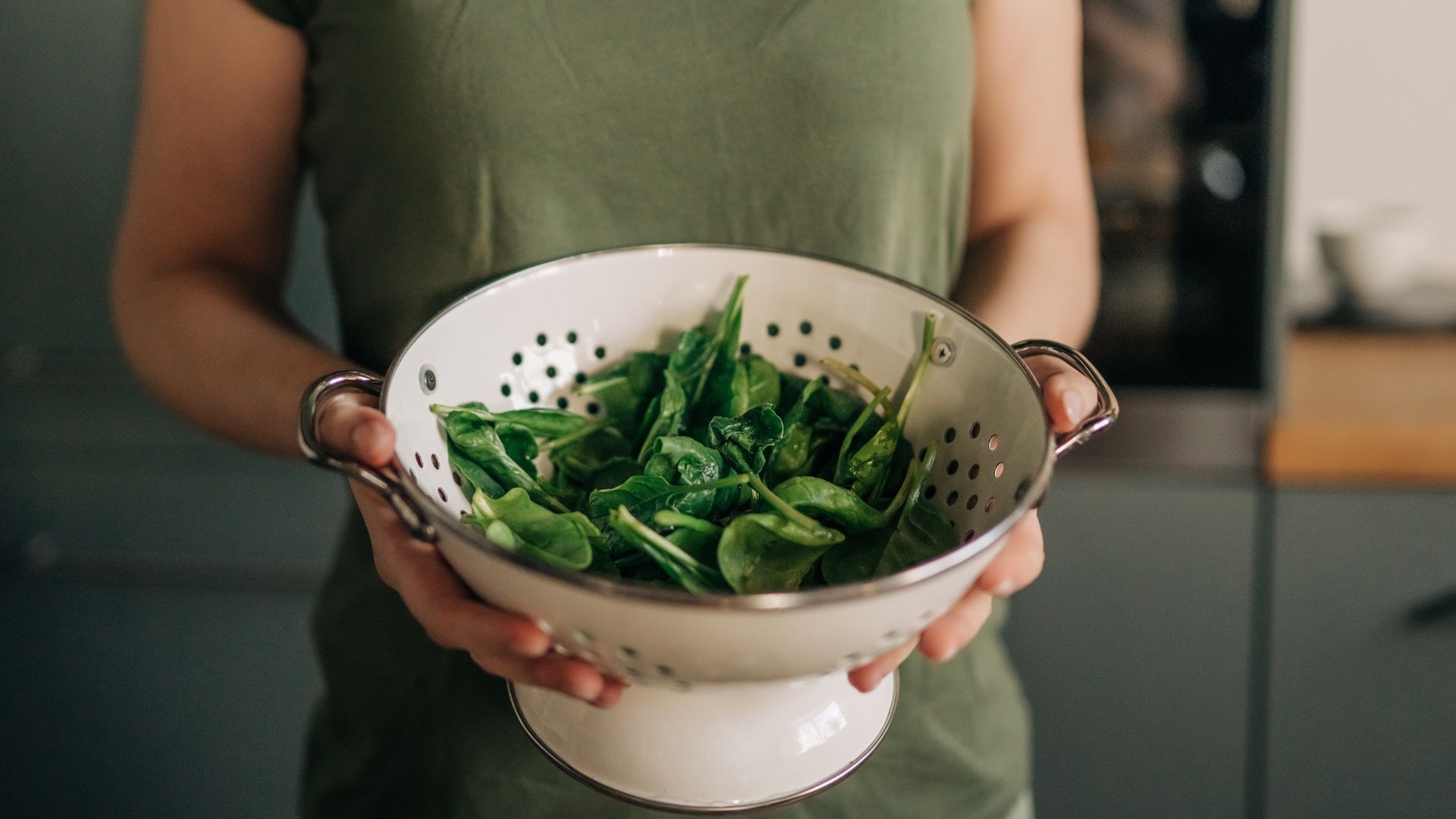Woman holding up a strainer full of spinach