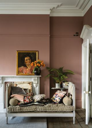 A pink living room using Farrow & Ball's Sulking Room – with a white chaise lounge, a white fireplace, elegant artwork, and a variety of flowers and potted plants