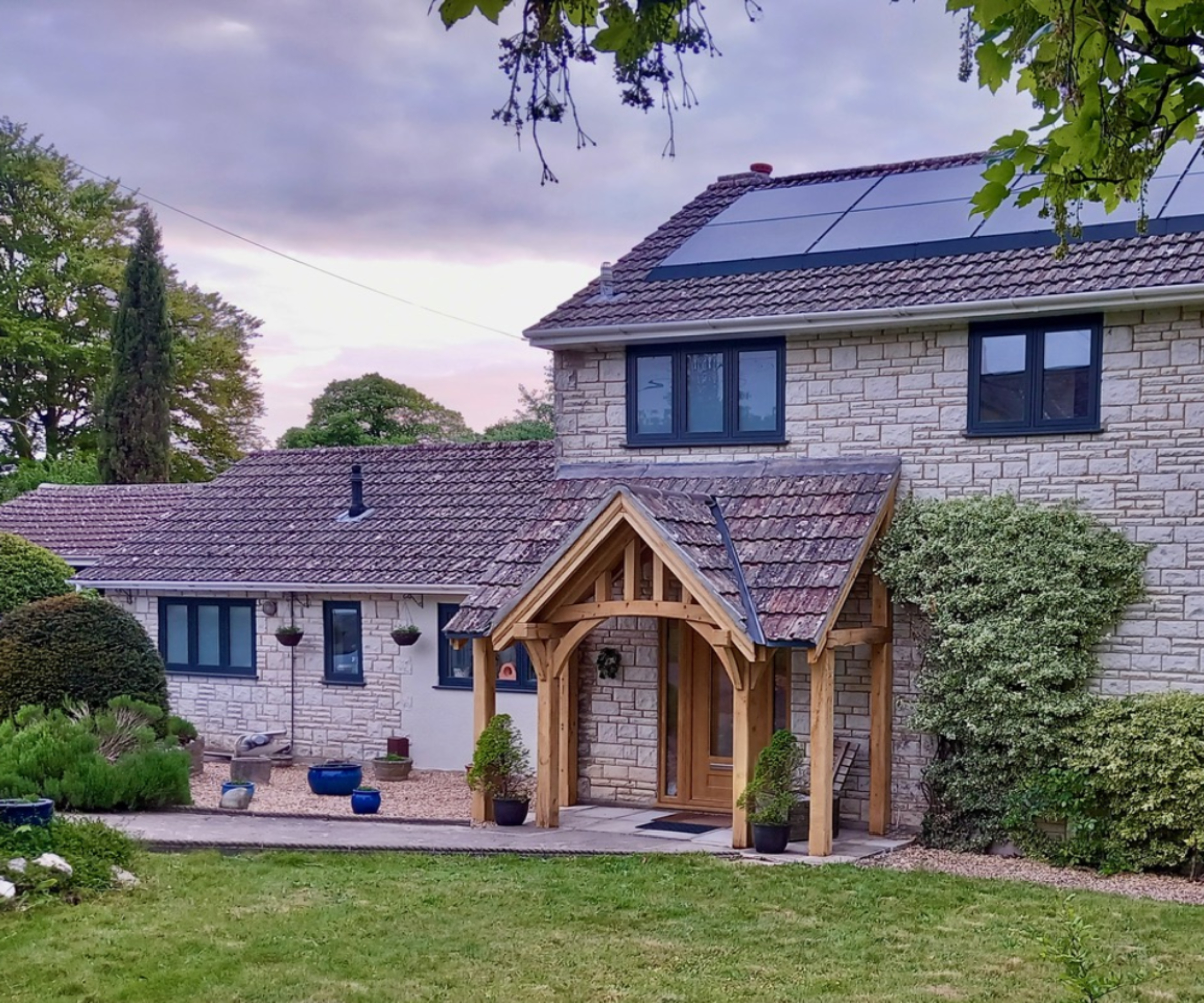 wide oak frame porch with tiled roof and an open sides and front on stone house with solar panels on roof