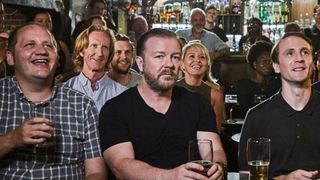 Sombre man sits among a group of smiling people in a pub