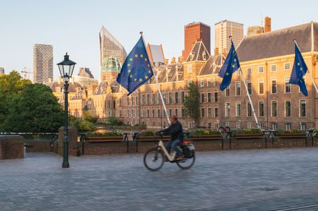 The Dutch parliament, also known as Binnenhof, in the city center of The Hague, Netherlands, behind a bridge with European Union flags and a man bicycling across it. 