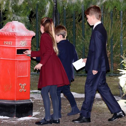 Princess Charlotte, Prince George and Prince Louis putting letters into a red mailbox next to a snowy tree