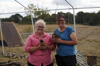 Grace and Dannie stand out in a field on their farm, each of them holding a chicken