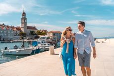 A joyful mature couple walking along the charming Adriatic coastal town, enjoying a sunny day.
