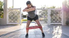 Woman in sportswear steps sideways with a resistance around her legs, just below the knees