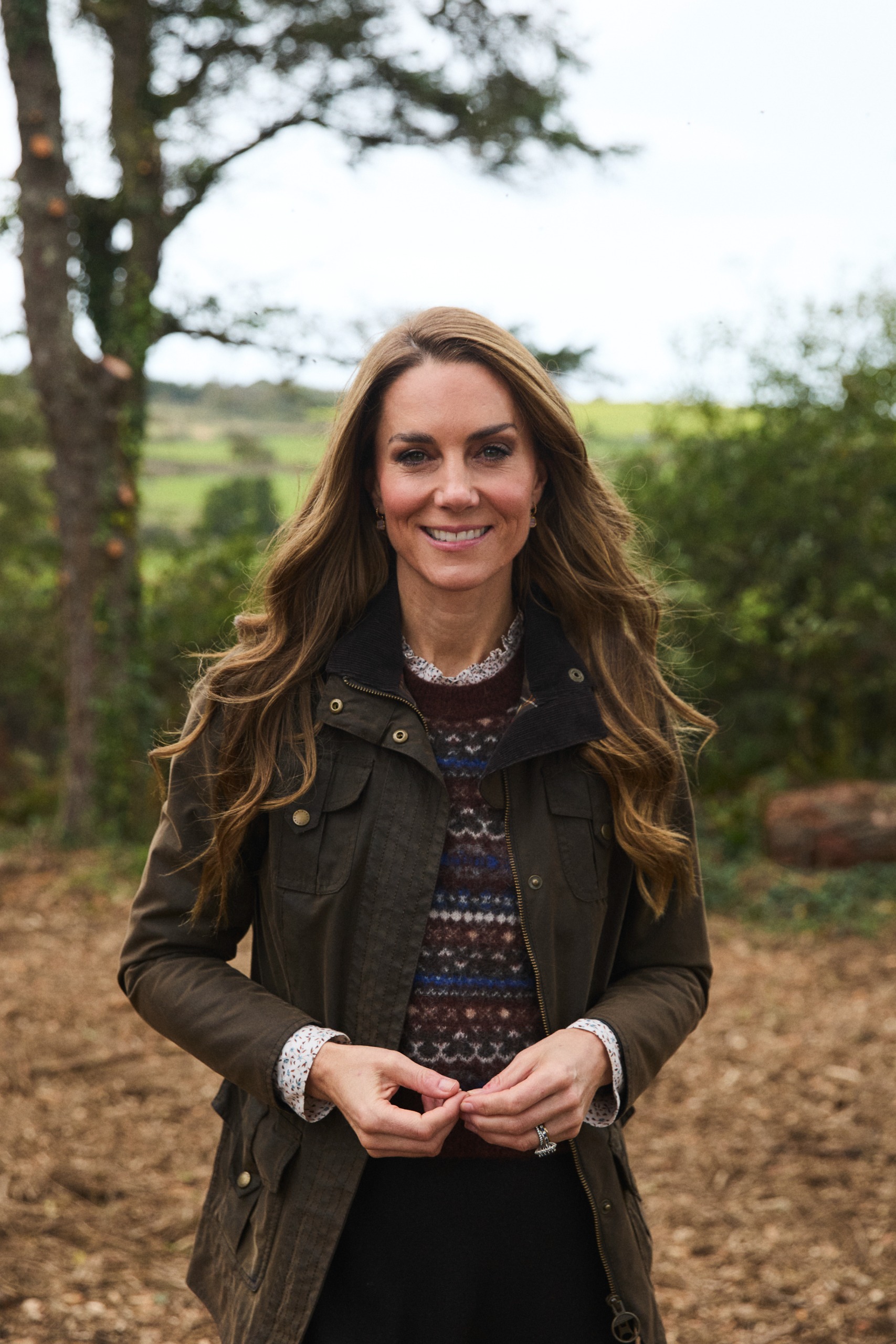 Princess Kate wearing a Fair Isle sweater and coat and smiling in front of trees