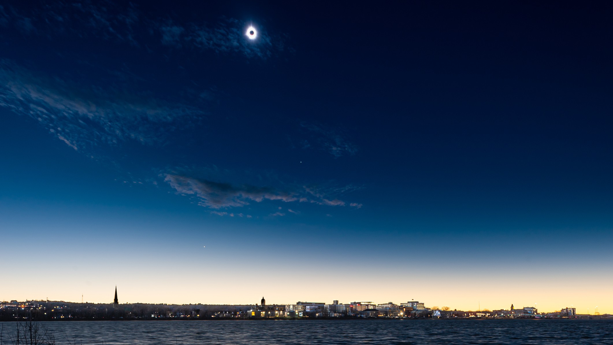 a total solar eclipse over a city scape in the distance, the sky is an deep inky blue color.