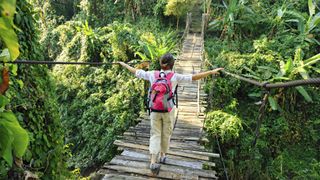 Woman with backpack on suspension bridge in rainforest by Fred Froese