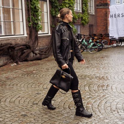  A guest wearing a black skirt, black sheer top, black leather jacket, black Hermes bag, and long shoes outside Herskind during the Copenhagen Fashion Week Spring/Summer 2024 on August 7, 2023 in Copenhagen, Denmark