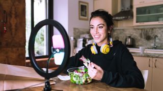 Woman eating a salad while on a video call with a ring light pointed at her