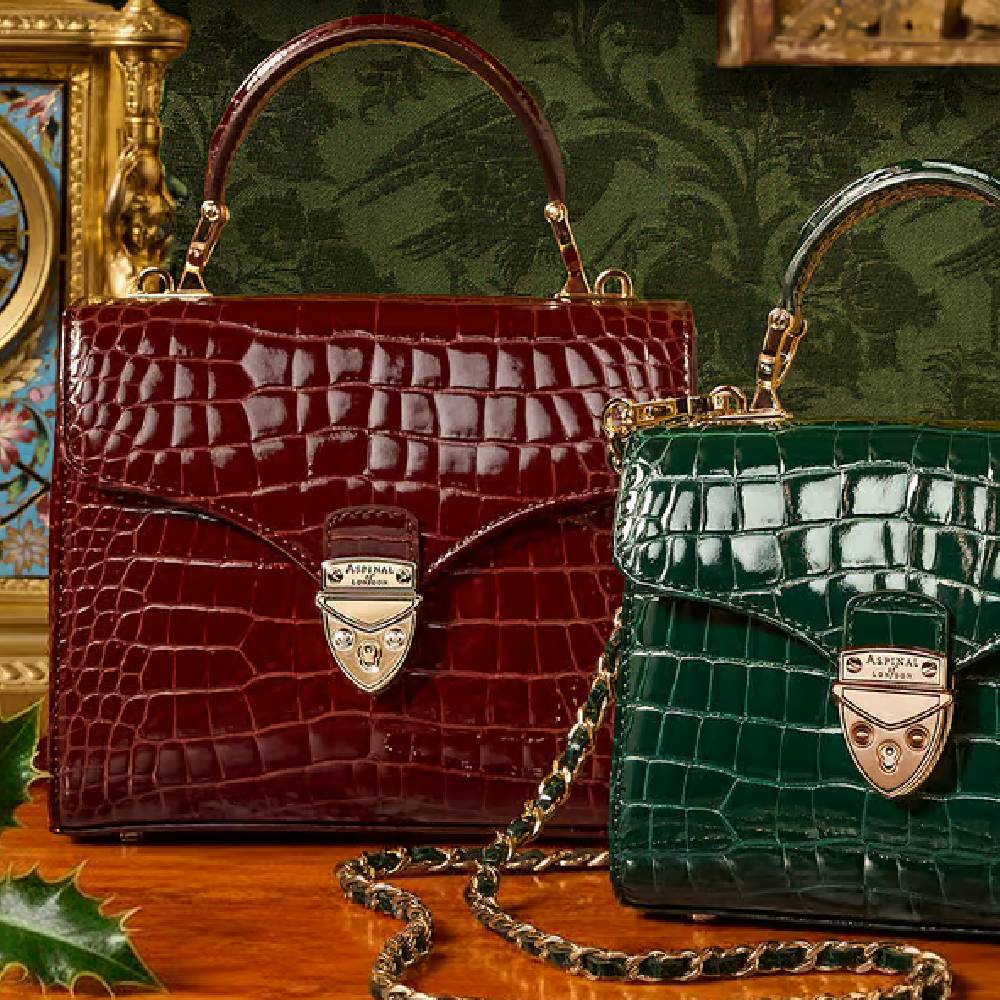 A deep red and deep green bag with gold detailing next to each other from Aspinal of London.
