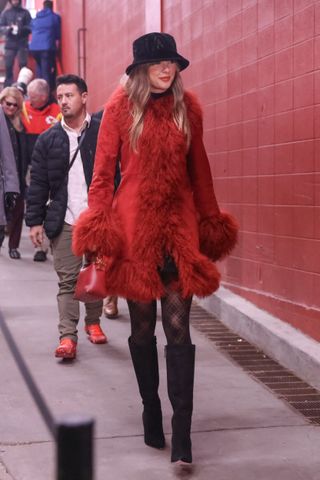 A photo of Taylor Swift wearing a red Charlotte Simone Penny Lane coat and black knee-high boots to a Kansas City Chiefs game on Dec. 21, 2024.