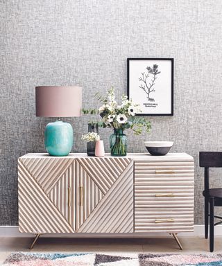 Grey living room ideas featuring a wooden sideboard with green lamp and grey textural wallpaper.