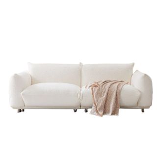 A white boucle couch with a beige throw