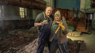 Keith Brymer Jones and Marj Hogarth in overalls stand in their chapel surrounded by rubble in Our Welsh Chapel Dream