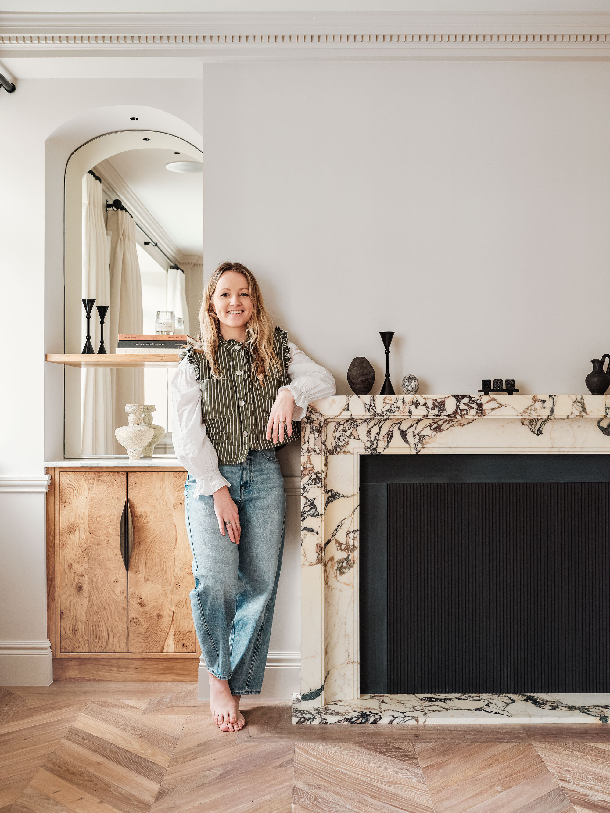 Designer Anna Moller standing next to a marble fireplace decorated with a mix of vases