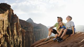 A family sits on a rock slab while hiking in Zion National Park, Utah