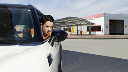 A woman adjusts the mirror of her car in a parking lot.