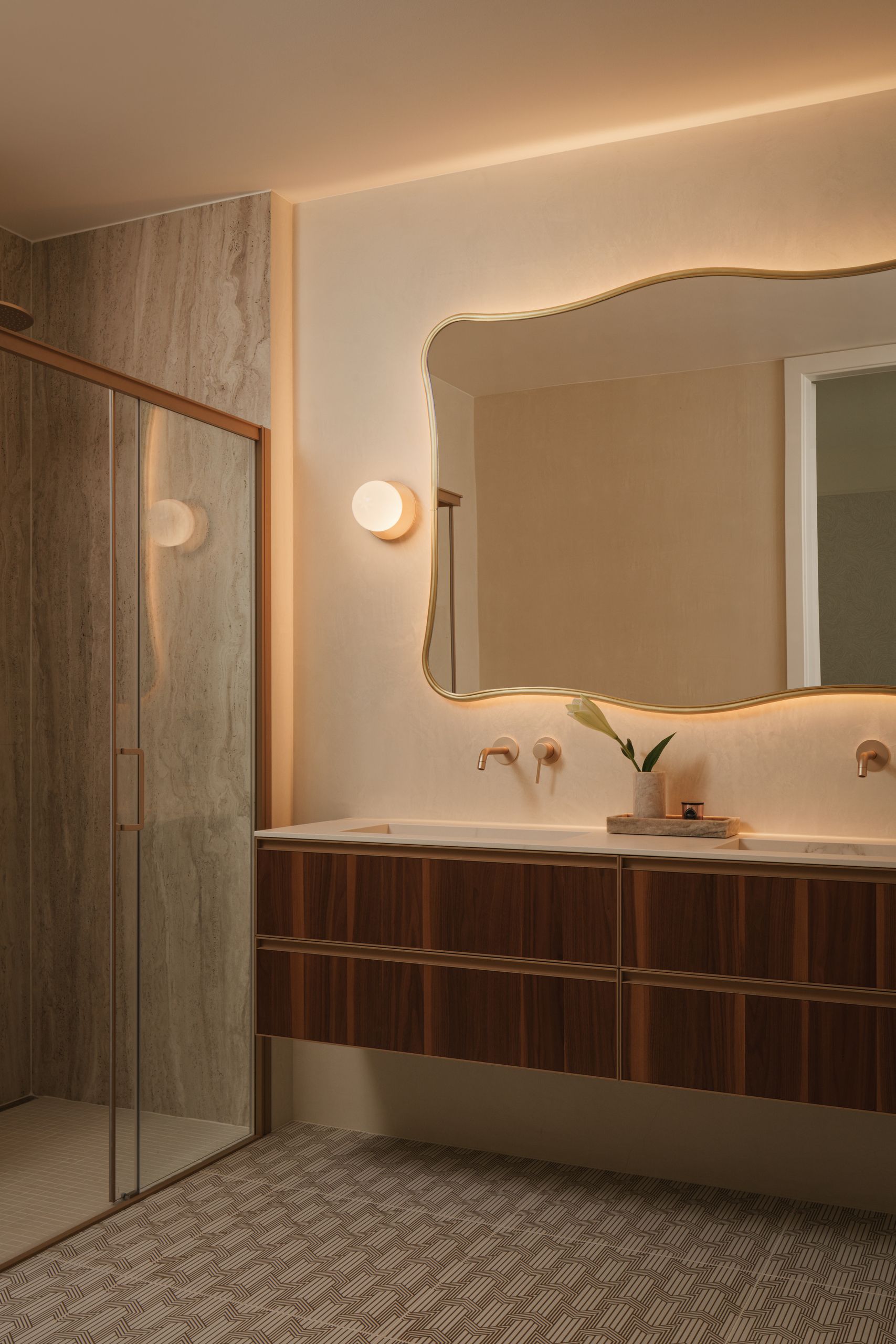 Image of a formal main bathroom with double sinks, a marble shower, wooden floating countertops and curved mirrors.