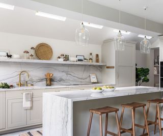 A neutral kitchen with white walls, taupe cabinets, marble-look countertops and a matching backsplash that ends with a cohesive floating shelf