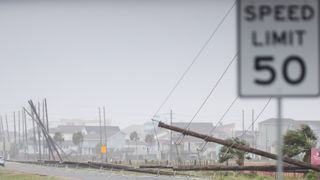 flood waters cover city streets as fallen power lines and damaged buildings can be seen in the background